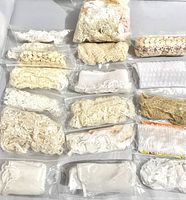 Top view of various small plastic bags each containing different lace trims and fabric bits in cream and off-white tones laid on a flat surface.