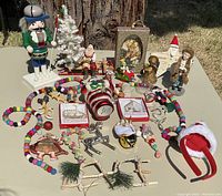 Photo showing most of the Christmas ornaments and decorations on a table, including nutcracker, felt bead garlands, Santa figures, boxed brass ornaments, and assorted holiday figurines.