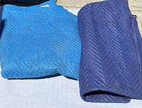 Two folded used moving blankets, one dark blue (72 x 80) and one lighter blue, both showing wear and dirt from use.
