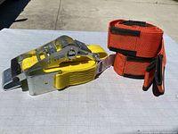 Coiled pair of red-orange padded forearm forklift straps with black Velcro and trim.