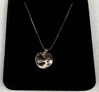 Sterling necklace with round sterling pendant featuring a small diamond, displayed on a black velvet-like background.