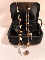 Necklace arranged inside black velvet box with drawstring pouch visible.