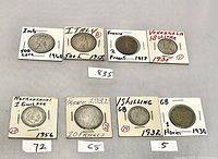 Photo showing eight vintage international coins in white cardboard holders with markings .835 and .72. Coins from France, Italy, Venezuela, Netherlands, and Great Britain are visible with dates and denominations.