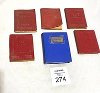Group of six small vintage books, five with embossed red leather covers and one blue hardcover book, displayed together on a white surface with auction catalog card.