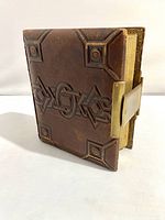 Front view of the vintage photo album showing molded leather cover with geometric pattern and metal lock.