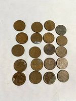 20 Wheat Back pennies arranged on a white cloth, showing mostly the reverse side with wheat ears and some obverse sides.