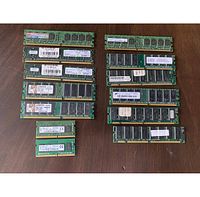 Photo of multiple old green PCB RAM modules of various sizes and types laid out on a wooden surface.