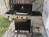 Front left angle view showing full grill with control knobs, side burner, and propane tank below.
