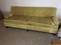 Front view of the vintage yellow velvet 3-seater couch on a beige carpet, showing the tufted back and solid wood legs.