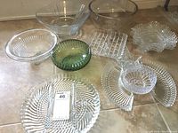 Overview of 9 glass items including bowls and dishes of various shapes and designs, placed on a flat surface.