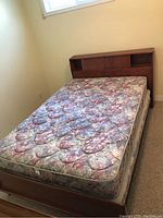 Double bed with solid maple headboard and footboard, featuring floral patterned mattress and boxspring, against beige wall under window