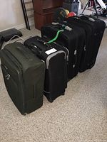 Set of four suitcases standing side by side on carpeted floor, showing size variation and color differences.