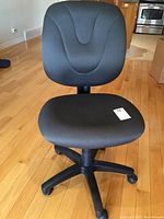Full view of black upholstered office chair showing seat, backrest, base, and caster wheels on wood floor.