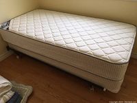 Full side view of single bed with mattress on platform metal frame with caster wheels. Light cream patterned mattress with edge piping.