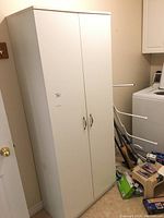 Front view of white storage cabinet in a laundry room, showing two doors with handles, some visible wear and staining.