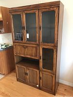 Full view of the retro wood wall unit showing both glass display cabinets on top and cane-front lower doors with the drop-down bar shelf section in the middle.
