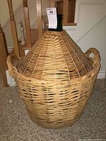 Front view of green glass carboy fully enclosed in a tightly woven wicker basket with rounded handles.