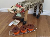 Photo of the folk art cat stool along with the condiment set and porcelain trivets on a wooden floor
