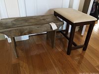 Two wooden stools on wood floor, one rustic garden stool/bench and one upholstered wooden stool