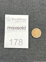 Photo showing Indian Head penny next to lot number card on black fabric.