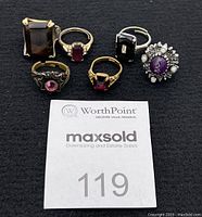 Six assorted cosmetic rings displayed on dark fabric with a WorthPoint Maxsold auction lot number 119 card.