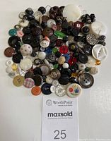 A top view of about 125 mixed vintage buttons including black, white, brown, and colorful examples in various materials and sizes clustered together for display.