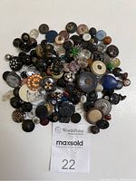Top-down photo showing a diverse assortment of approximately 147 vintage buttons in various sizes, designs, and materials scattered on a flat surface.