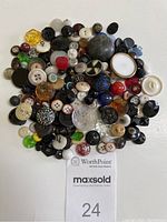 Top-down view of approximately 160 assorted vintage buttons of multiple colors and materials, spread flat on white background.