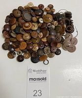 Top-down view of about 170 brown vintage buttons arranged on a white surface showing variety of styles, sizes, and some with old thread attached.