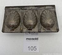 Closed antique metal mold with three shell-shaped cavities visible on exterior side, showing its aged surface and hinge line.