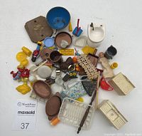 Top-down photo of the entire lot showing random assortment of small plastic and ceramic dollhouse kitchen accessories including miniature sink, cookware, birds, and other items.