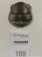 Photo of a silver-tone metal badge with embossed U.S. Capitol dome and 'METROPOLITAN POLICE' text. Number '31' at bottom.