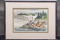 Framed watercolour painting of lakeside scene with rocks and trees.