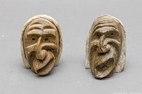 Two small brownish stone carvings showing Native American faces with distinct carved and painted features, front view.