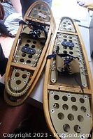 Two pairs of wooden snowshoes laid side by side showing bindings and decking material.