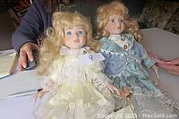 Two antique Sabre Porcelain collector dolls sitting on a table, both with blonde hair and original clothing, as described by seller.