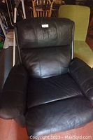 Front view of black leather recliner chair showing cushioned back, seat, and armrests.