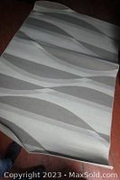 Carpet folded to show pattern and texture details, displaying wave-like design in gray and off-white.