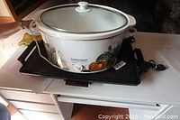 Top view of Hamilton Beach slow cooker with fruit decoration and glass lid on black tray