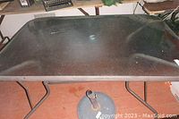 Top view of rectangular patio table with glass top and black metal frame, showing wear and dust.