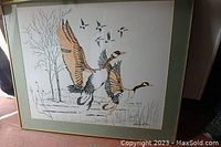 Framed watercolour artwork showing two geese flying in front of a background with a tree and grasses.