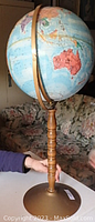 Full side view of standing globe showing the wooden stand and brass meridian with Australia prominently visible on the globe.