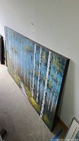 Side angle view of the large canvas painting leaning against a wall showing birch trees with blue sky.