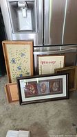 Group photo showing multiple framed prints and painted wood trays leaning against refrigerator