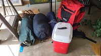 Full overview of camping items including backpack, cooler, tent bag, mattress, sleeping bag, and cutting tool.