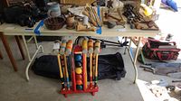 Photo showing the white folding catering table with various woodworking tools, a mechanical device, and croquet set below.