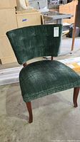 Angled front-side view of green upholstered chair with button tufting and wooden legs, showing some wear and veneer loss.