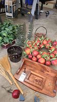 Faux leafy plants, faux fruit wreath, metal planter, woven basket, wooden tray with hooks, straw brooms, and decorative metal coat hooks on floor