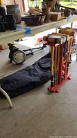 Collapsible manual golf club cart, Kourt King croquet set with mallets, balls, and red wooden stand, and black fabric golf bag base with wheels visible