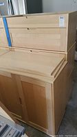 Three Ikea armoire pieces disassembled shown stacked together with one piece front visible showing wood doors and drawers.